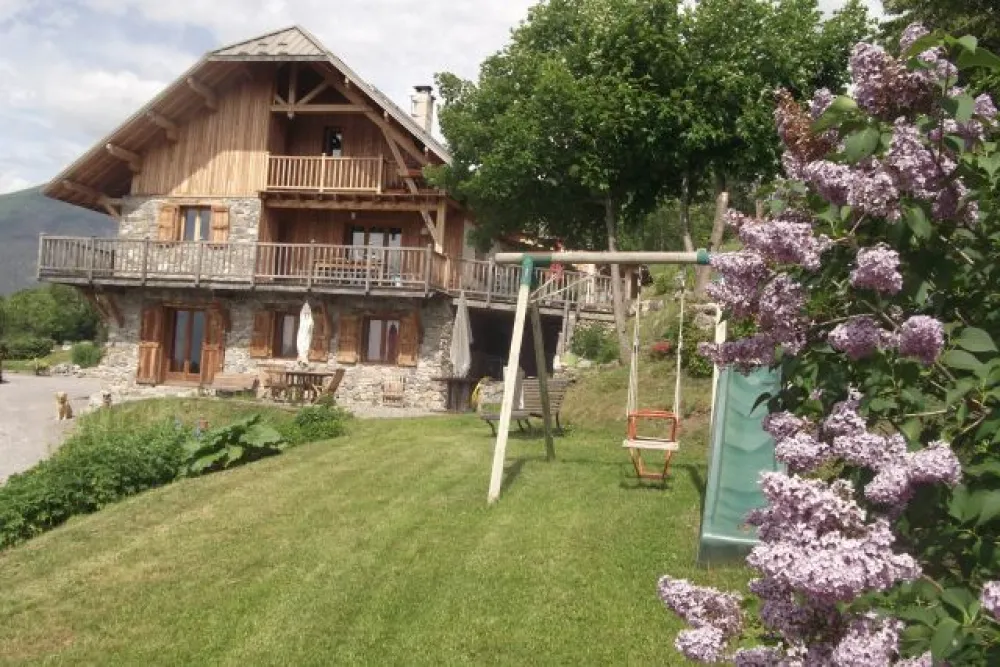 Vue de la maison en été avec l'espace jeu, balançoire, hamac, banc...