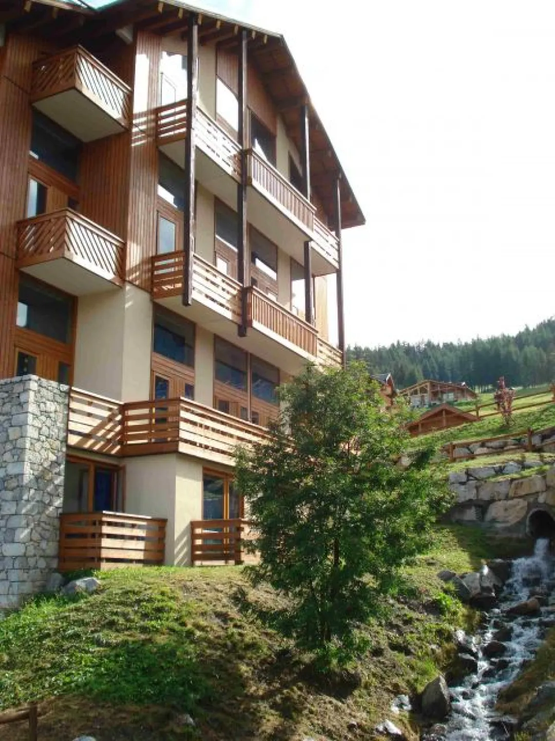 View of the residence on summer, with the little stream. The apartment is the balcony at the top center.