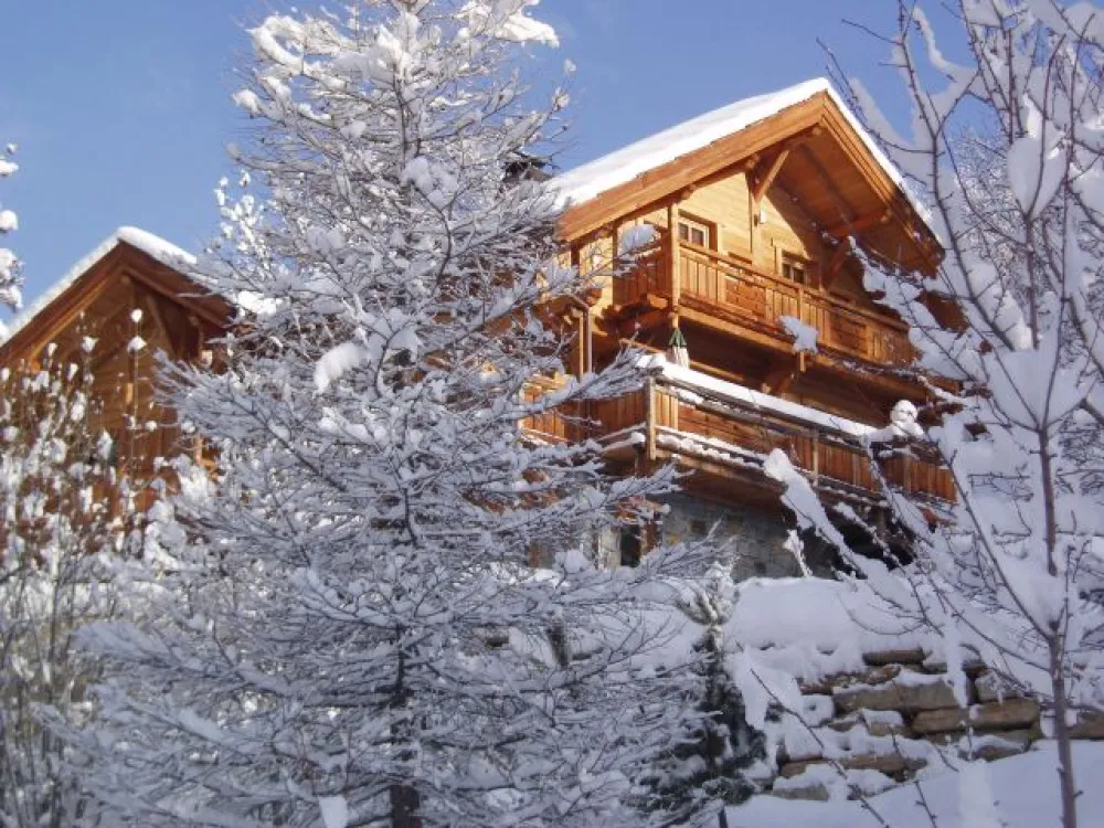 Hiver : Chalet "l'Ourson Blanc" sous la neige, réalisé par le constructeur "Bayrou", tout en mélèze de pays, avec le soubassement en pierres et la toiture en bardeaux de mélèze