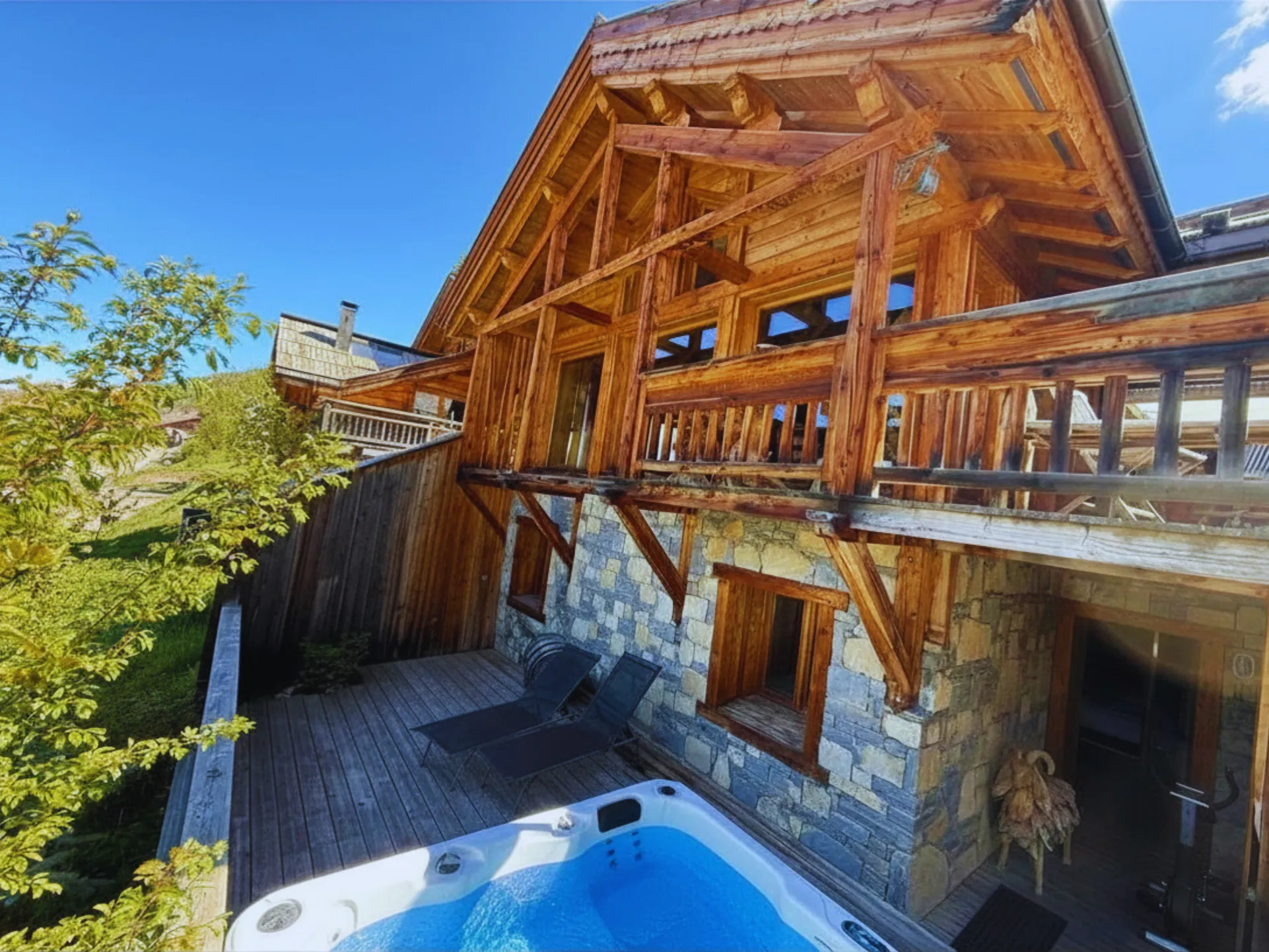 Photo graphique de la façade ouest en pierre et bois du Chalet B à Vars, mettant en valeur une partie de la terrasse avec ses transats et son jacuzzi.