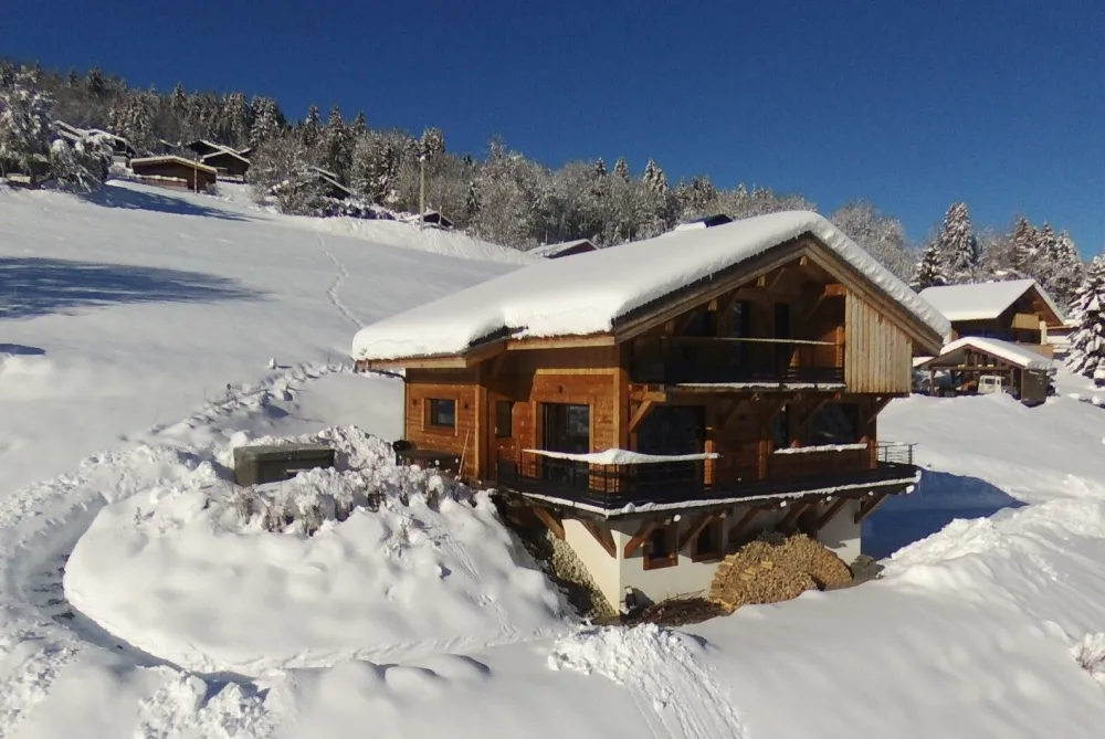 Façades Est et Sud du chalet "Le Flocon" et sa terrasse avec spa en hiver.