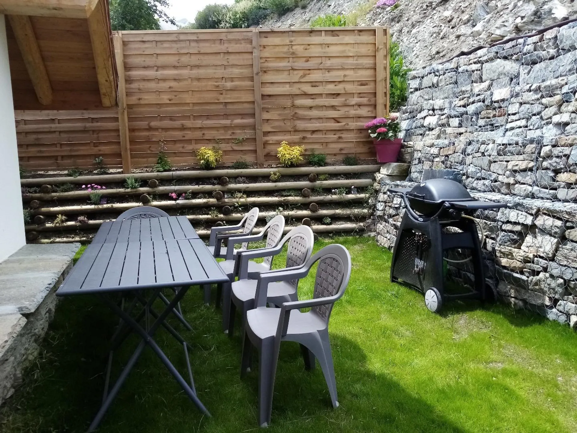 Jardin à l'arrière du chalet au niveau de la pièce à vivre avec Barbecue WEBER et chaises longues