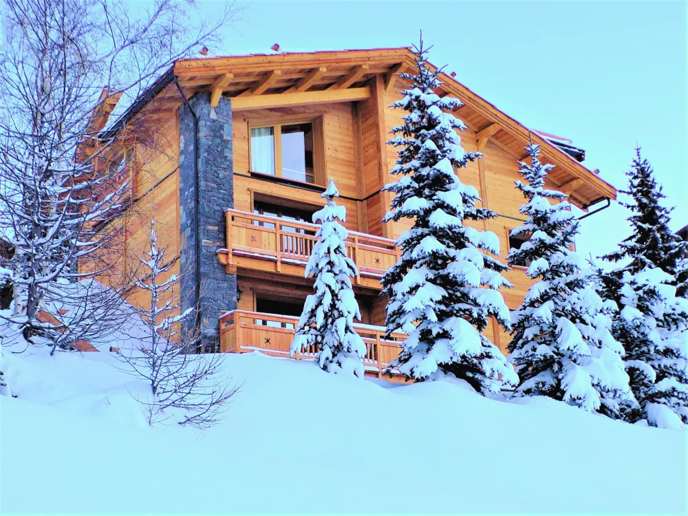 Grande façade Ouest en vieux bois et pierre du Chalet Kergwen à Montgenèvre, entièrement recouverte de neige en hiver.