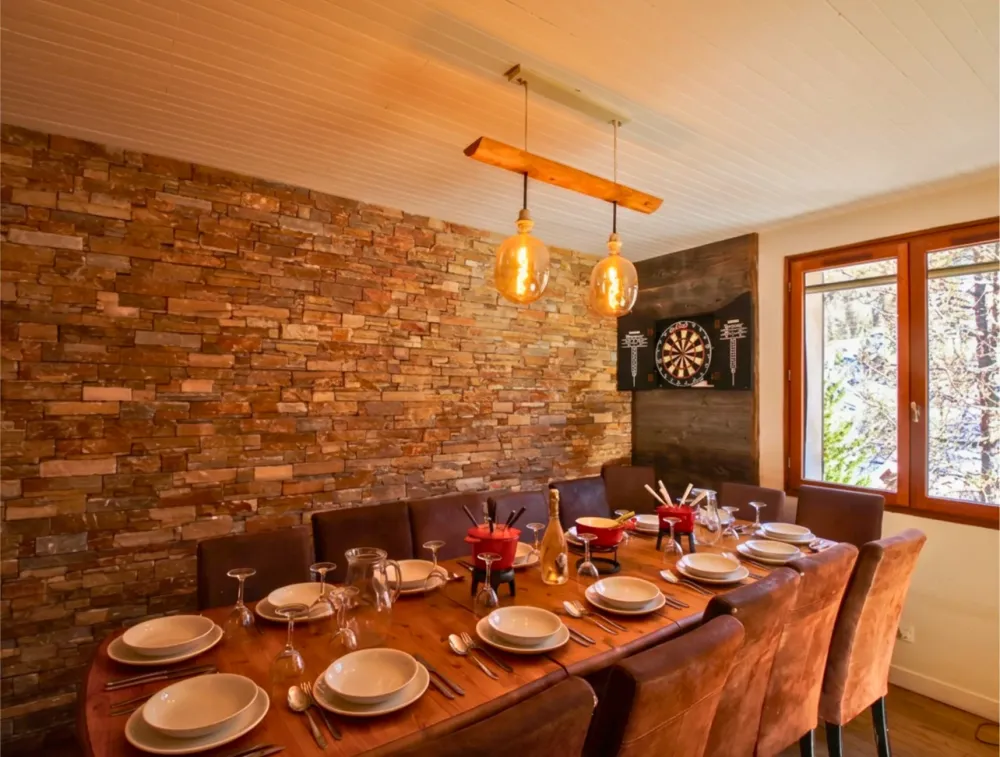 La table est soigneusement dressée pour un repas de groupe accueillant jusqu'à 14 personnes. Des appareils à fondue sont disposés au centre, illustrant l'expérience chaleureuse et conviviale d'un séjour aux sports d'hiver en famille ou entre amis.