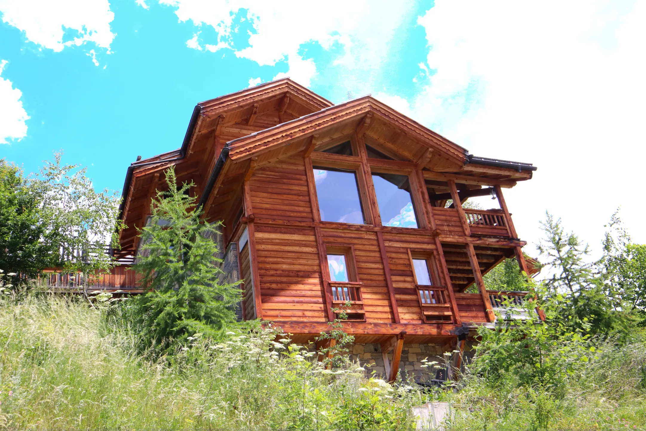 La façade du e-chalet mêle bois et pierre avec de grandes baies vitrées, offrant un style chaleureux et moderne à la montagne.