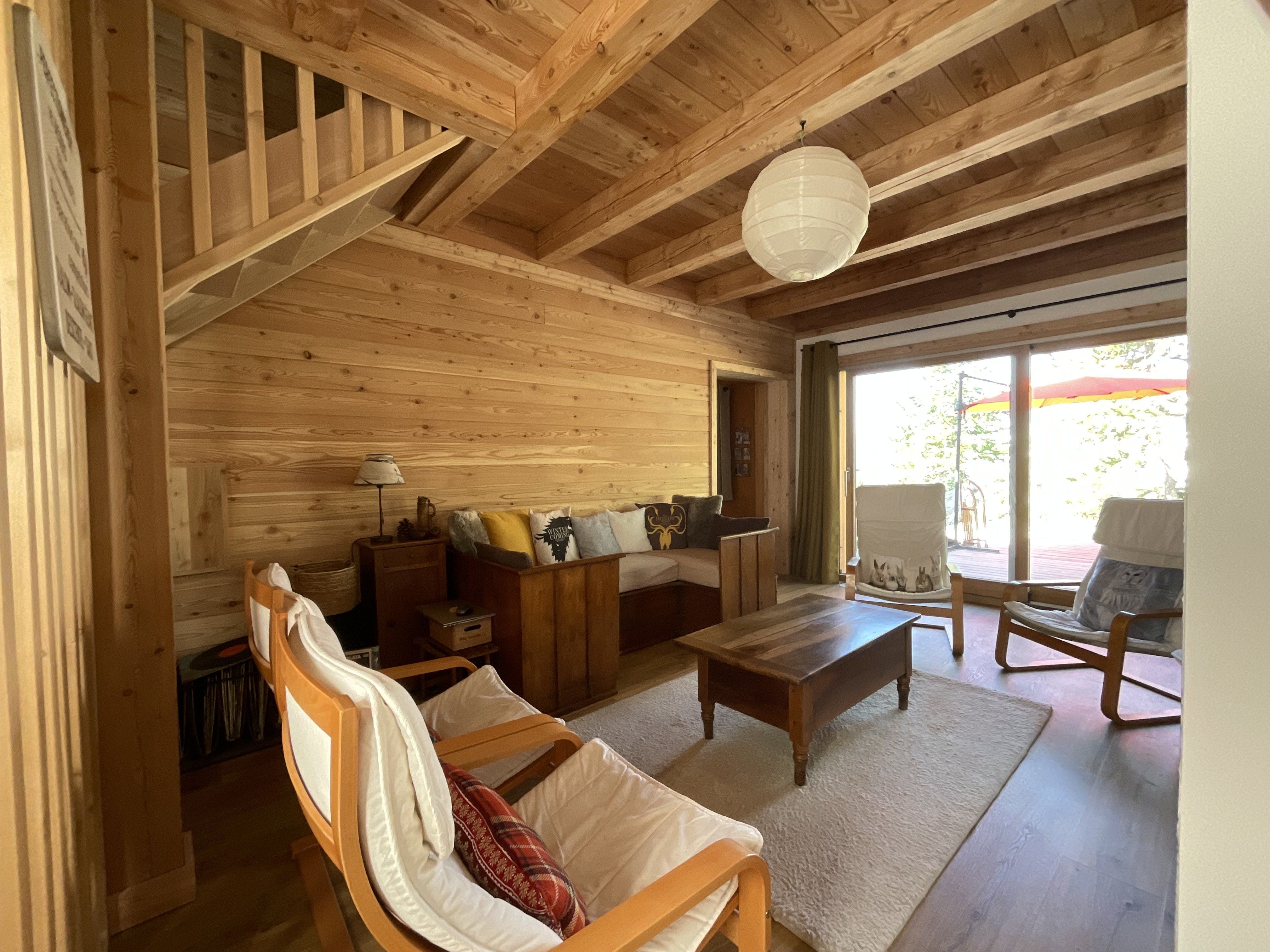 Une autre photo du salon qui bénéficie d'une belle vue par la large baie vitrée et qui communique avec la salle à manger par une porte coulissante. L'escalier monte vers une chambre double avec balcon et une salle de bains