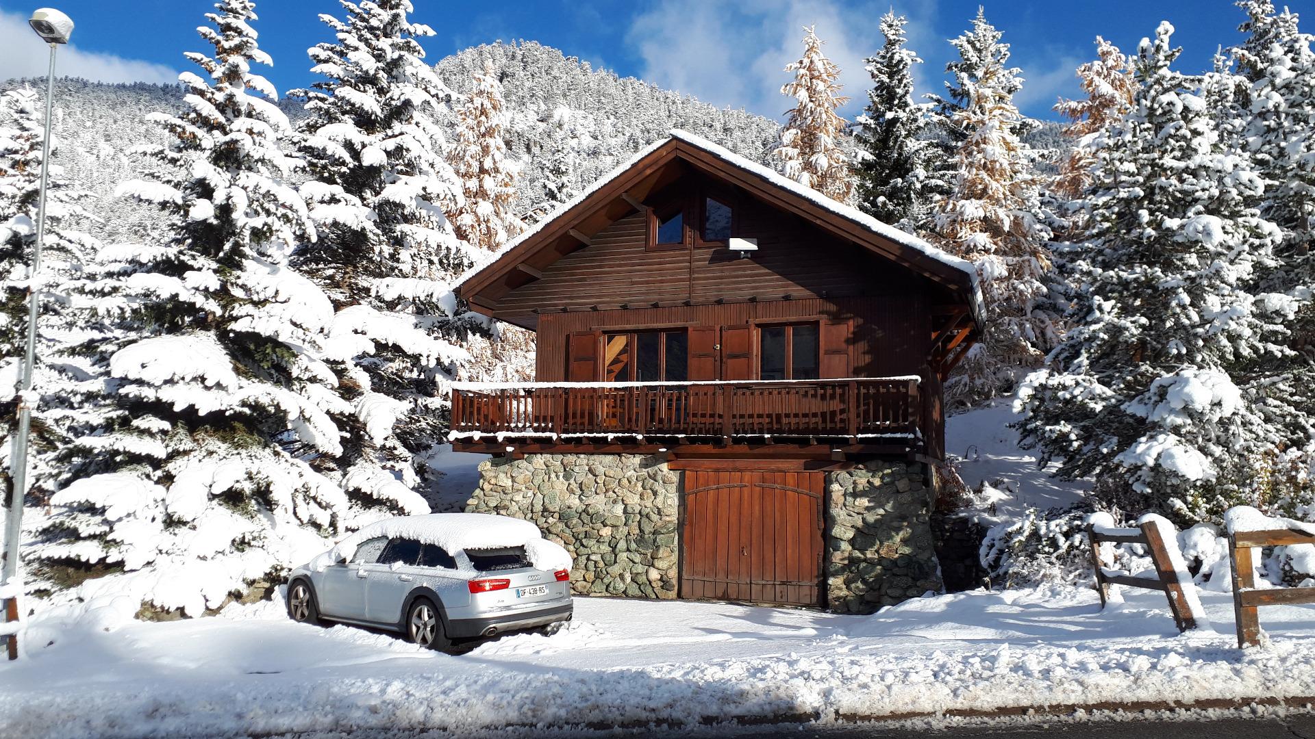 Vue de face du chalet, niché dans les arbres, bénéficiant de 3 places de de parking privées 