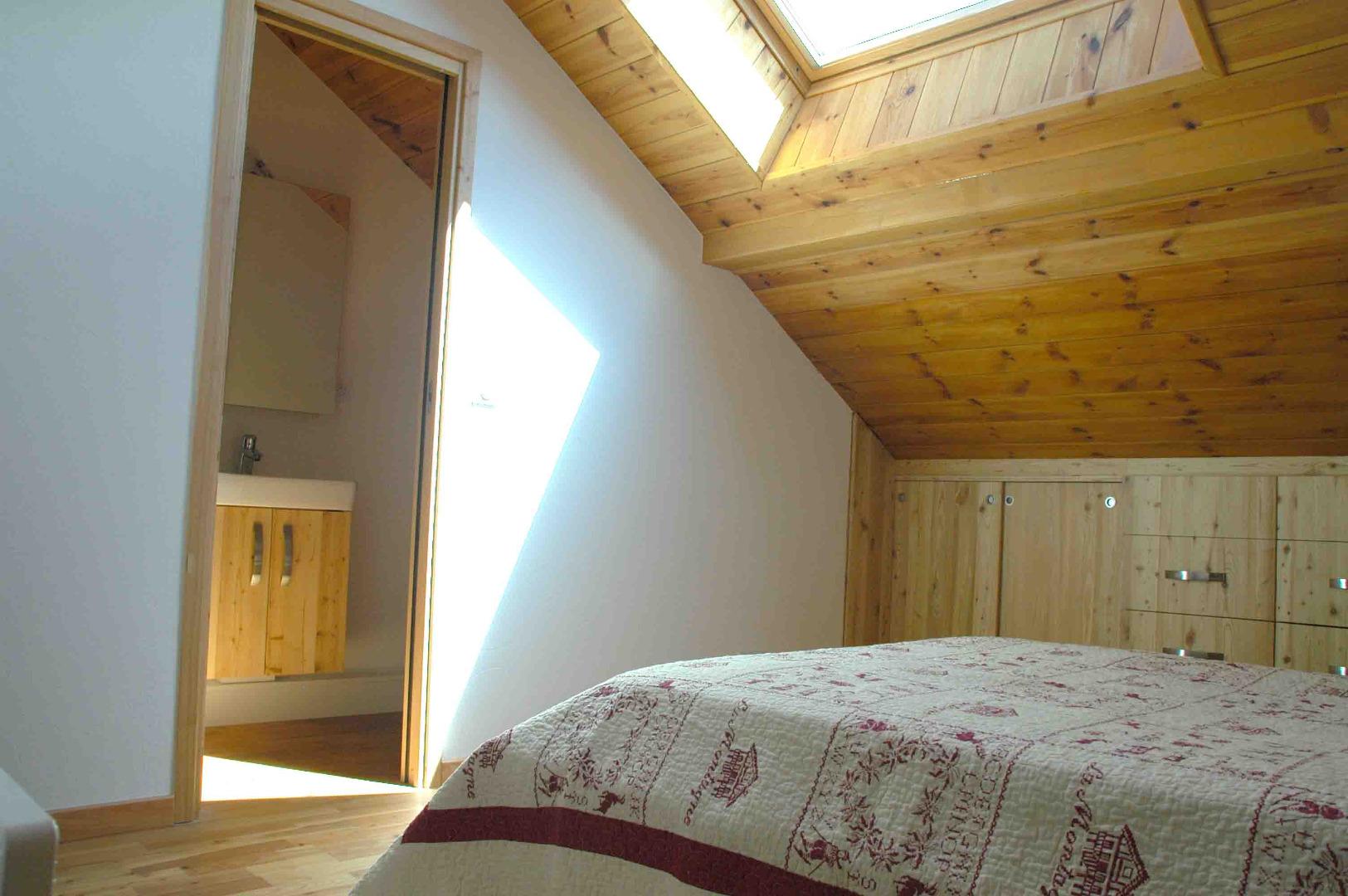 Vue transversale de la Chambre parentale en mezzanine avec lit de 140, rangements et salle d'eau privée (douche, lavabo et WC suspendu)