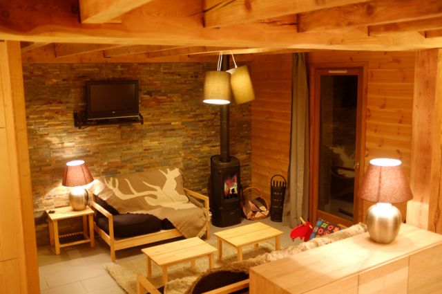 Espace salon conçu avec poutres apparentes, pierres et bois. Aménagé d'un poêle à bois (bois à disposition) et une TV écran plat.