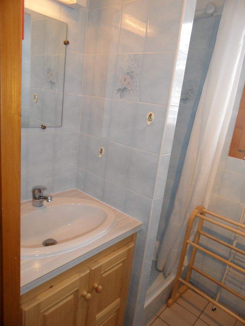 Salle d'eau avec douche et vasque sur meuble, petite fenêtre avec volets.
