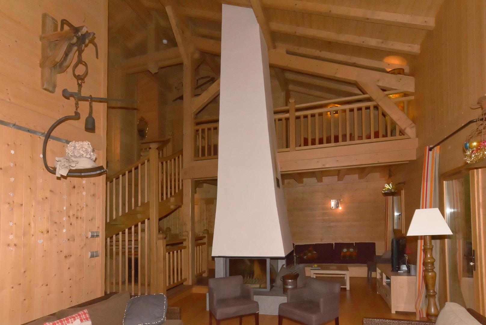 Niveau 2. Vue d'ensemble du salon, du salon TV, de la cheminée centrale (vitrée sur 4 faces), de la mezzanine et de l'escalier qui conduit aux chambres (vers le haut) et vers le studio( vers le bas).