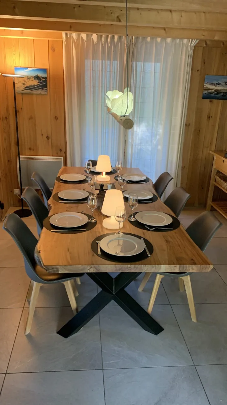 Skis à peine rangés, la table en acacia massif se pare pour le dîner. Bougies allumées, verres qui s'entrechoquent, dix couverts prêts à accueillir les récits de la journée. Chaque soir, le cœur du chalet.