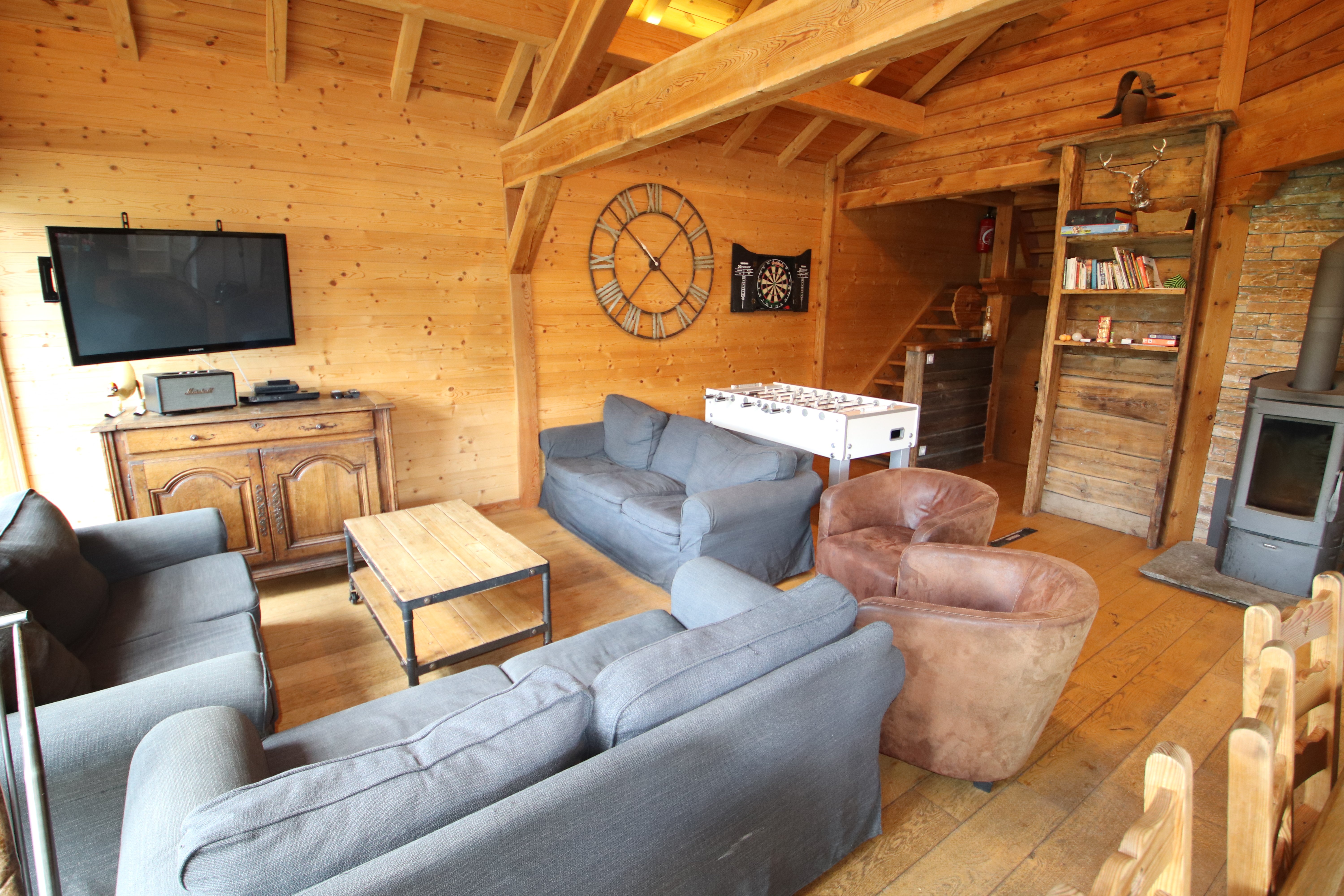 Grand salon sous toit cathédrale du Chalet B à Vars avec poêle à bois, canapé en U, TV écran plat, baby-foot et jeu de fléchettes.
