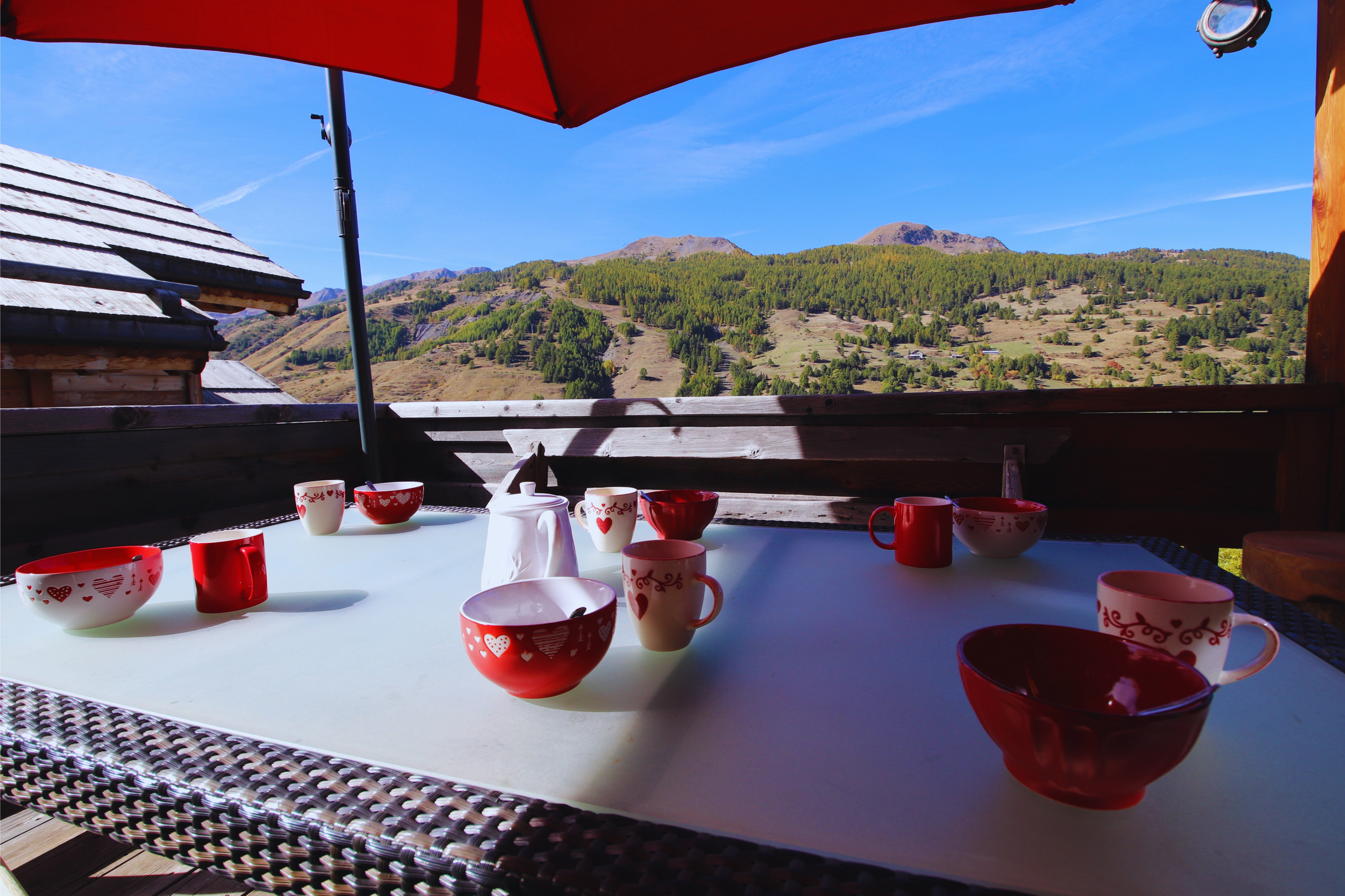 Table extérieure dressée pour le petit-déjeuner sur la terrasse du Chalet B à Vars, au niveau de la cuisine et du salon, avec la montagne en arrière-plan.