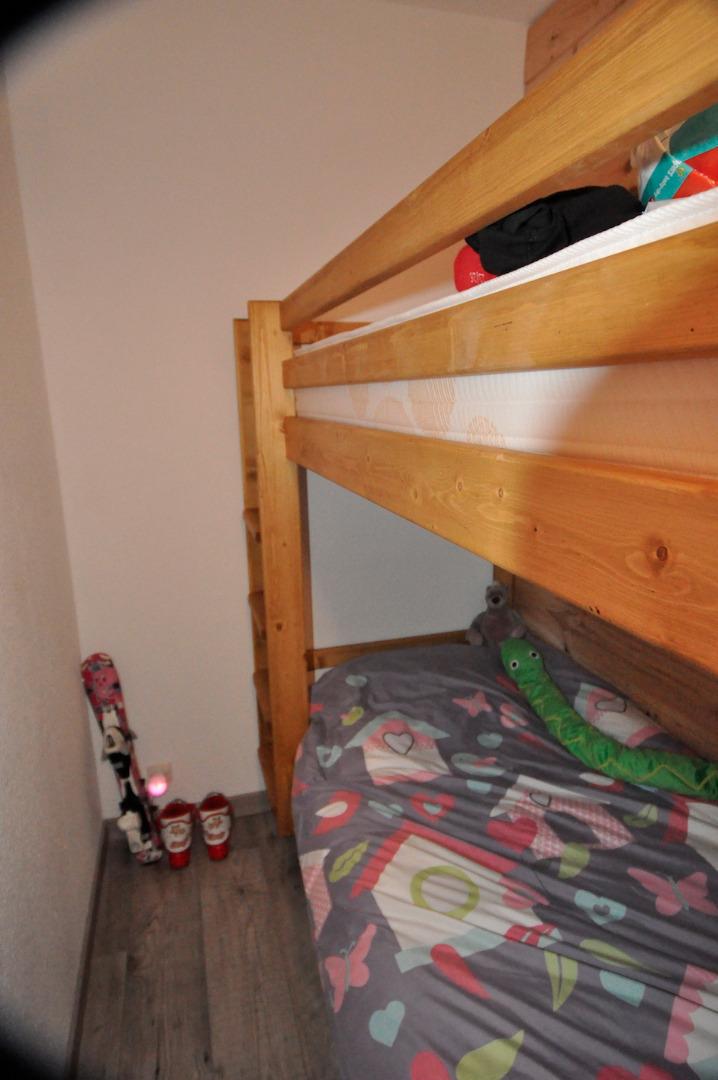 Deux lits superposés dans une pièce fermée. Sous le lit, deux tiroirs. en bout de lits, des rangements, une penderie enfant. 