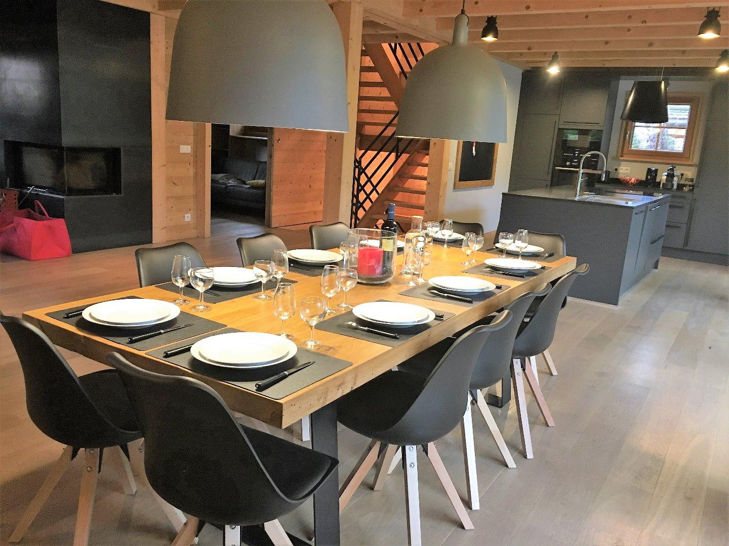 La salle à manger et sa grande table en chêne massif donnant sur la cheminée et la cuisine. Idéale pour des repas chaleureux autour d'une raclette ou d'une fondue savoyarde !