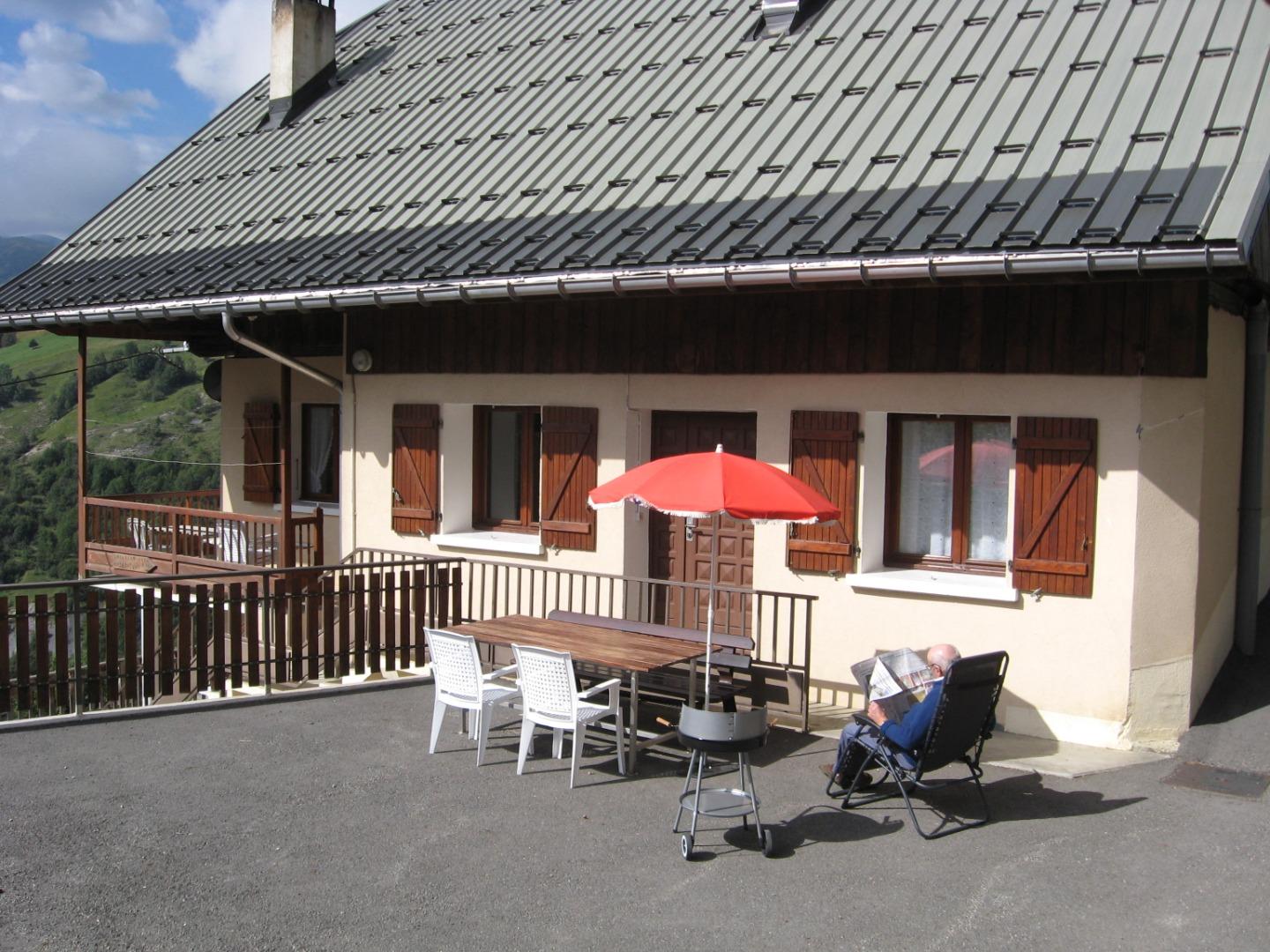 Devant l'appartement : table, parasol, chaises, barbecue...