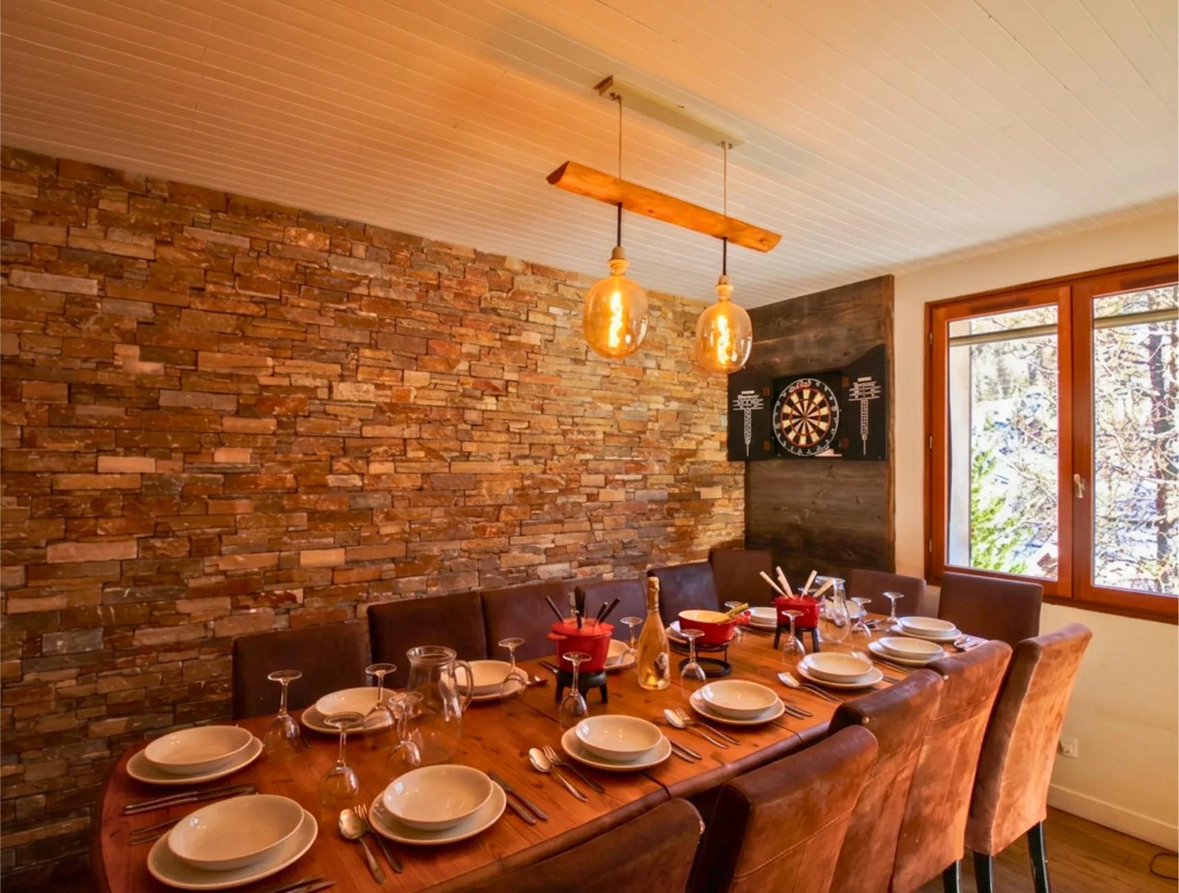 La table est soigneusement dressée pour un repas de groupe accueillant jusqu'à 14 personnes. Des appareils à fondue sont disposés au centre, illustrant l'expérience chaleureuse et conviviale d'un séjour aux sports d'hiver en famille ou entre amis.