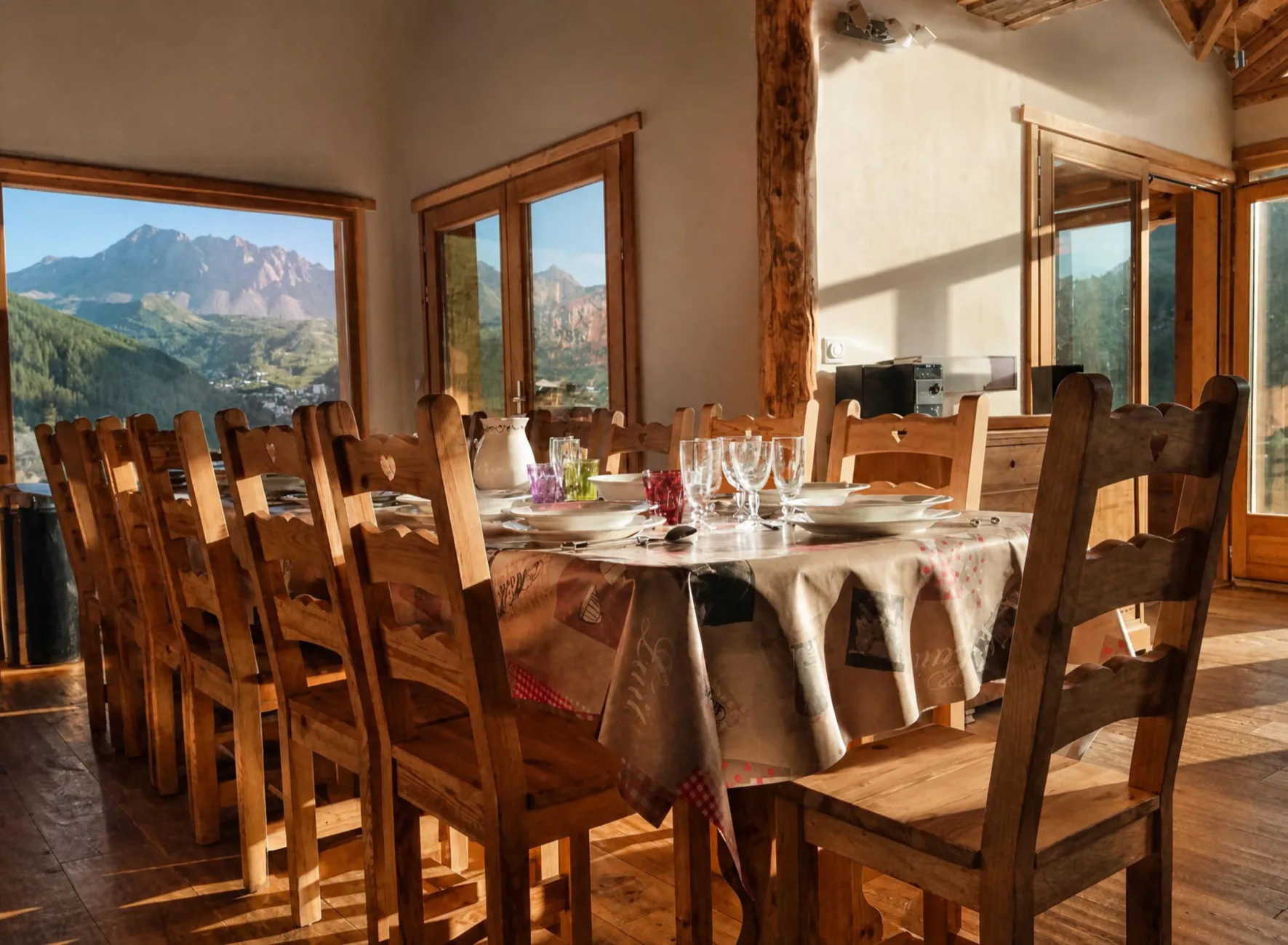 Grande salle à manger du Chalet C à Vars, avec une table dressée au complet pour 14 personnes autour d'une fondue savoyarde. De larges baies vitrées offrent une vue panoramique sur les montagnes et la crête de l'Eyssina.