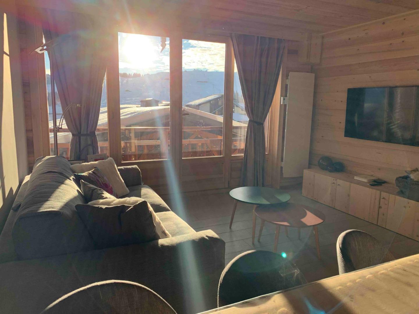 Salon cosy, en hiver avec Soleil avec la vue sur le mont Bisanne et les pistes. TV 4K, Apple TV, Amazon Prime Video, Netflix, Wifi debit Fibre, et canapé premium.