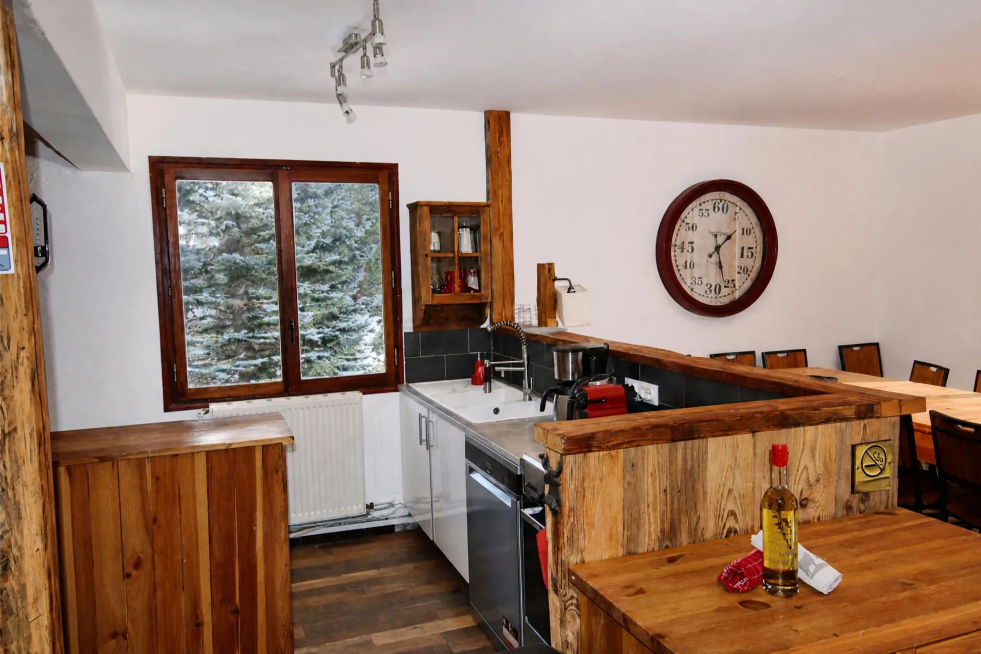 Cuisine équipée en bois du chalet La Soldanelle à Montgenèvre avec lave-vaisselle, four, machine à café, bar et fenêtre sur les sapins